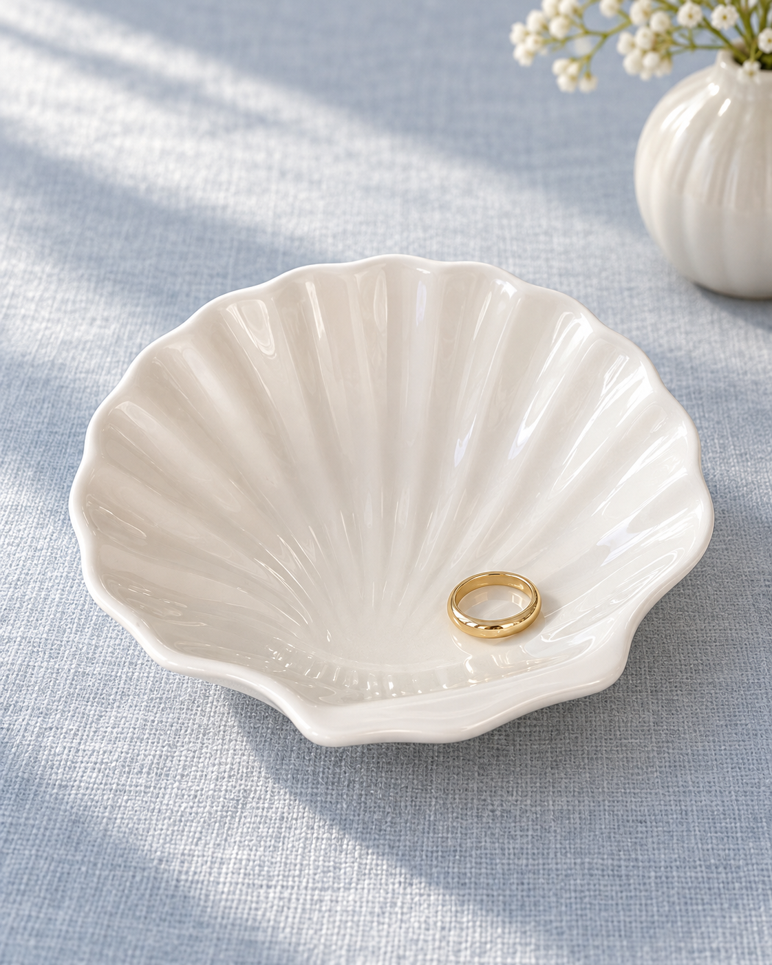 White shell-shaped ceramic dish holding a ring on blue fabric