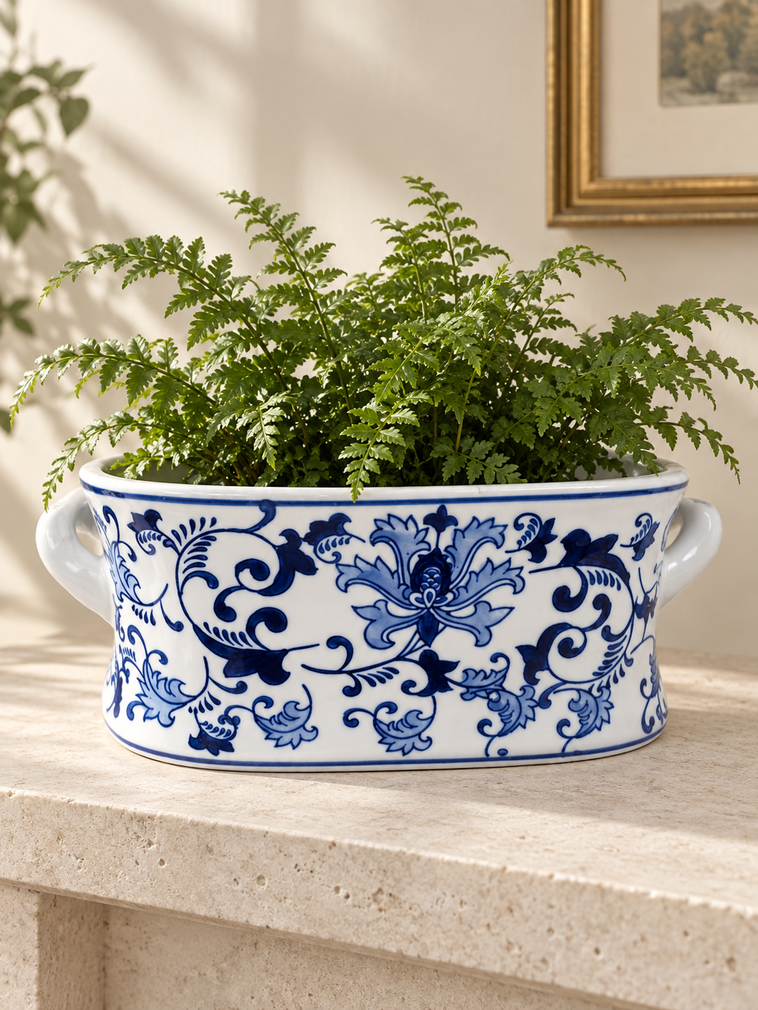 Blue and white oval planter with floral scrolls and side handles, styled with a fern