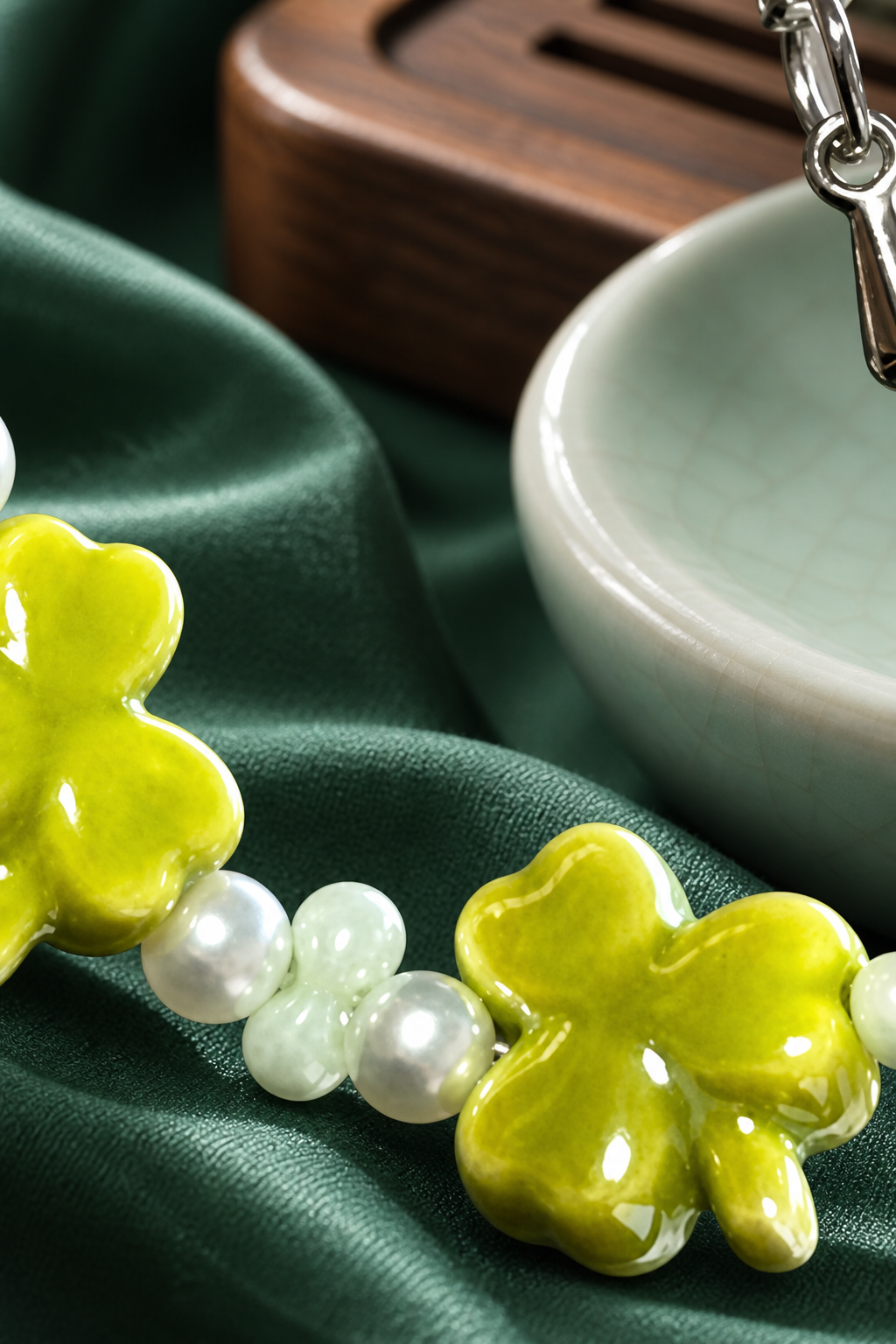 Close-up of glossy green clover shapes and pale bracelet beads